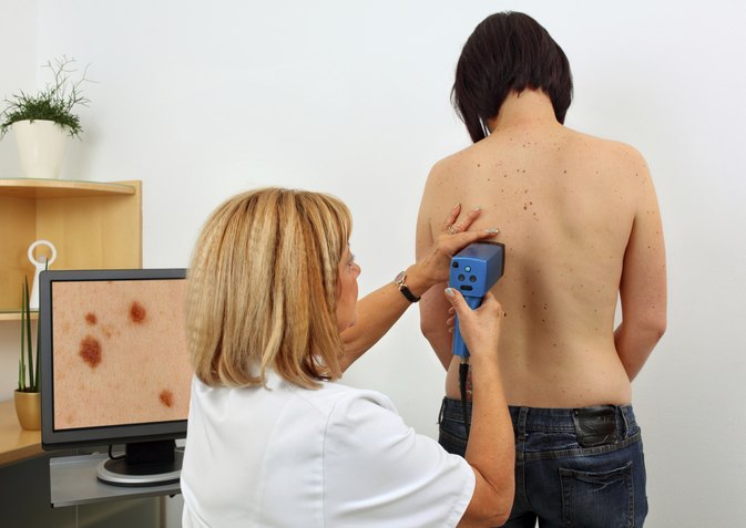 A woman is using an electronic device to check the skin of a man.