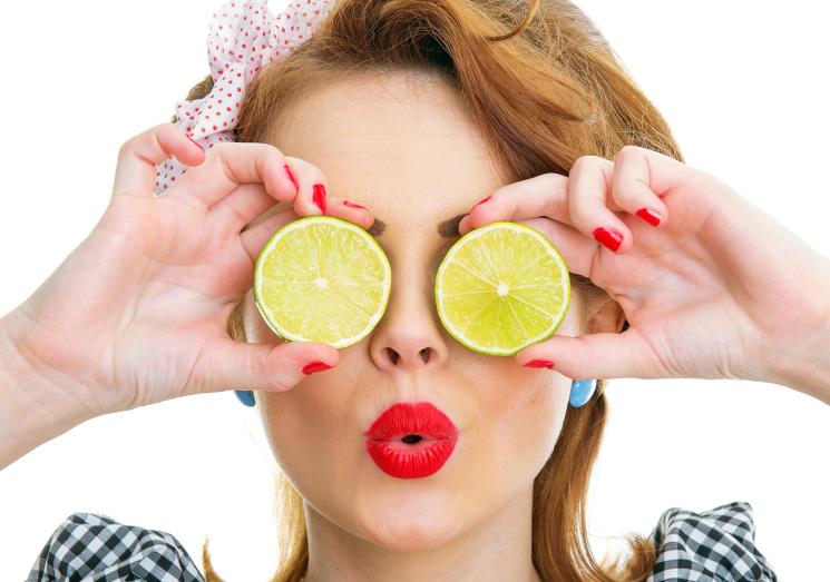 A woman holding two slices of lime in front of her eyes.