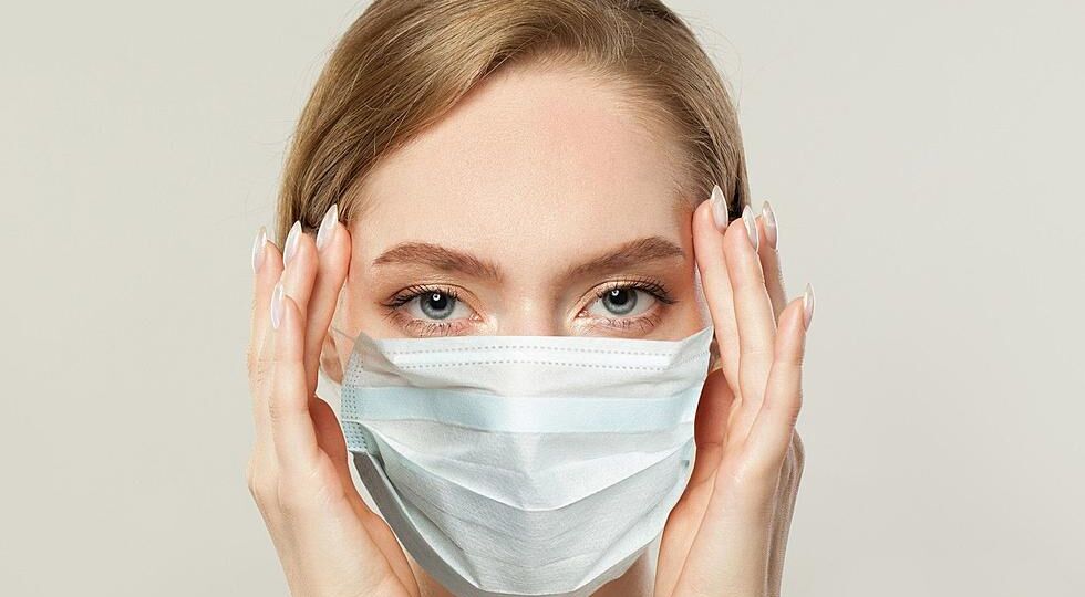 A woman wearing a face mask with her hands on the side of her face.