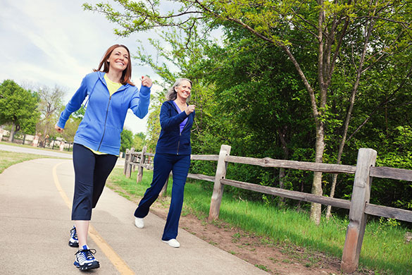 Two women are riding a skateboard down the road.